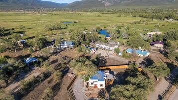 An aerial view of a rural property with multiple buildings, including a main house with a blue roof, surrounded by trees and open fields.