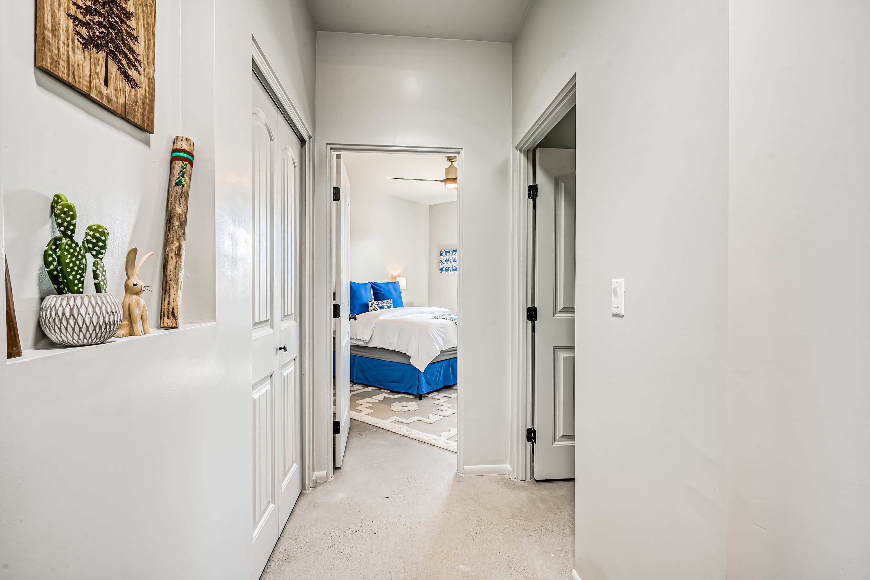 A hallway leading to a bedroom with a bed, a ceiling fan, and a wall-mounted cactus.