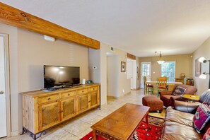 A living room with a wooden TV stand, leather sofa, and a dining area with a table and chairs. - Closson Charmer - Courtyard & Steps to Railyard (Santa Fe)