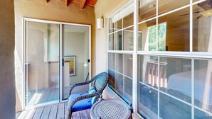 En balkon med en fletstol og et rundt bord, en skydedør i glas samt et stort vindue.