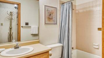 A bathroom with a sink, toilet, shower, and a framed picture on the wall.