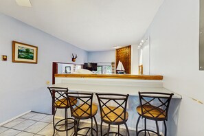 A kitchen with a white countertop, a wooden backsplash, and a window. There are four bar stools with cushioned seats. - Angel Fire Chalet 51 - Walk to Ski, Bike & Dining (Angel Fire)