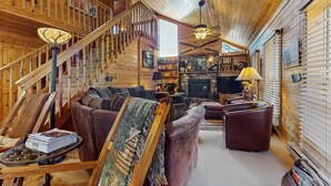 Ein Holzblock-Interieur mit Treppe, Ledersofas, Kamin und Fernseher.