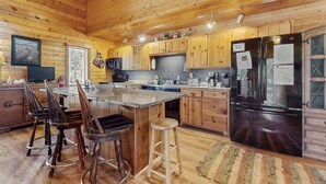 Ein Interieur einer Holzhütte mit einer Küche, die eine große Kochinsel, Barhocker, einen Kühlschrank und Holzschränke umfasst.