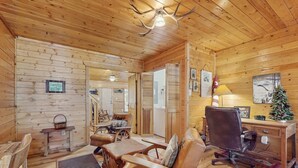 Ein Holzblockhaus-Interieur mit Essbereich, einem Wohnzimmer mit Sofa und Sessel, einem Schreibtisch mit Lampe sowie einem Weihnachtsbaum.