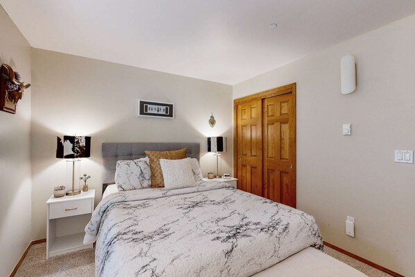 Ein Schlafzimmer mit einem Bett, Nachttischen, einem Wandbild, einer Holztür und einem Lichtschalter.