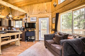 Interior d'una cabana de fusta amb cuina, zona de menjador i un sofà al costat d'una finestra gran.