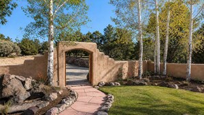Un sentier mène à une entrée en arc de cercle, bordée d’un jardin aménagé avec des rochers et des arbres.