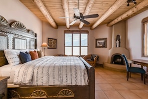 A bedroom with a bed, a ceiling fan, a fireplace, and a window.