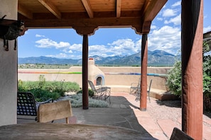 A covered patio with a view of mountains, a rustic wooden ceiling, and outdoor seating.