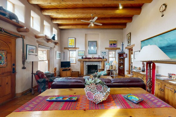 Ein geräumiges Wohnzimmer mit Holzboden, einem Kamin, einem Fernseher und einer Essecke mit farbenfrohem Teppich.