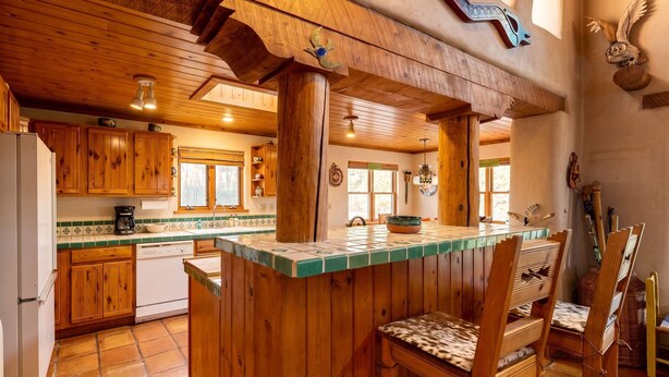 A rustic kitchen with wooden cabinets, a tiled backsplash, and a central island with bar stools. - Adobe Retreat - Walk to Plaza, Fireplace, Patio (Taos)