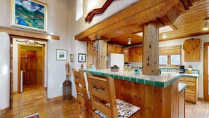 A rustic kitchen with wooden cabinets, a green-tiled island, and a wooden ceiling. - Adobe Retreat - Walk to Plaza, Fireplace, Patio (Taos)