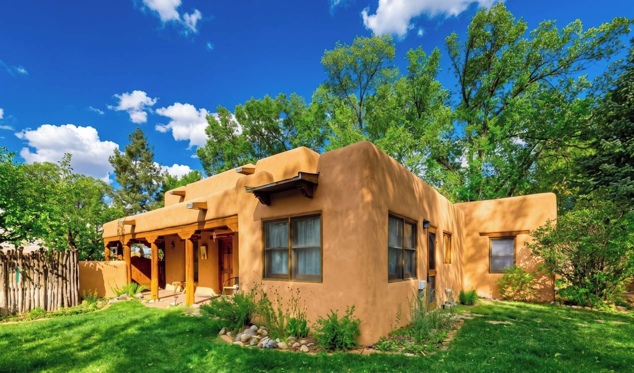 A single-story adobe-style house with a covered patio, surrounded by a well-maintained lawn and trees.