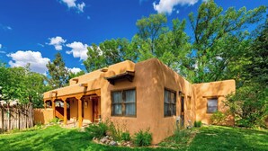 A single-story adobe-style house with a covered patio, surrounded by a well-maintained lawn and trees. - Adobe Retreat - Walk to Plaza, Fireplace, Patio (Taos)