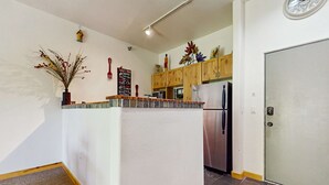 A kitchen with wooden cabinets, a refrigerator, a clock, and a decorative plant. - Sweet Retreat - Ski Valley Condo, Gym, Game Room (Taos Ski Valley)