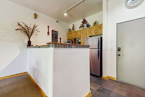 A kitchen with wooden cabinets, a refrigerator, a clock, and a decorative plant.