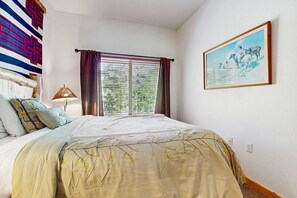 Un dormitorio con cama, ventana con cortinas, lámpara, un cuadro en la pared y un tapiz de pared con diseño.