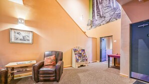 A lobby with a leather chair, a small table, a framed picture, a magazine rack, and a door. - Sweet Retreat - Ski Valley Condo, Gym, Game Room (Taos Ski Valley)