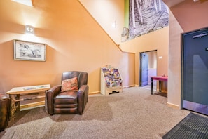 A lobby with a leather chair, a small table, a framed picture, a magazine rack, and a door.