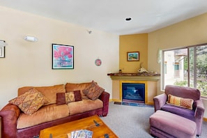 Una sala de estar con sofá, sillón, chimenea y ventanas amplias.