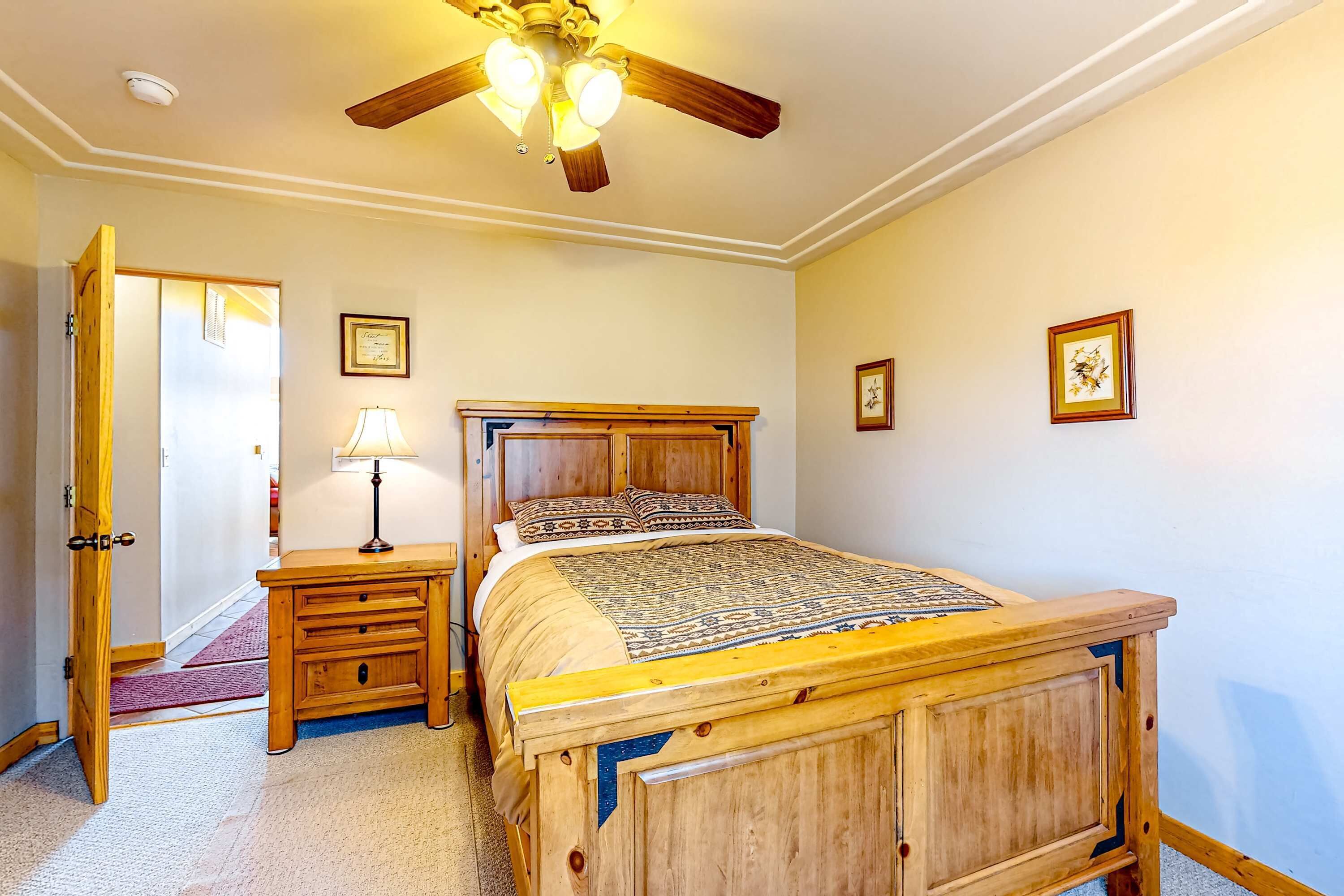 Une chambre à coucher avec un lit en bois, une table de chevet, un bureau, un ventilateur de plafond et une porte.