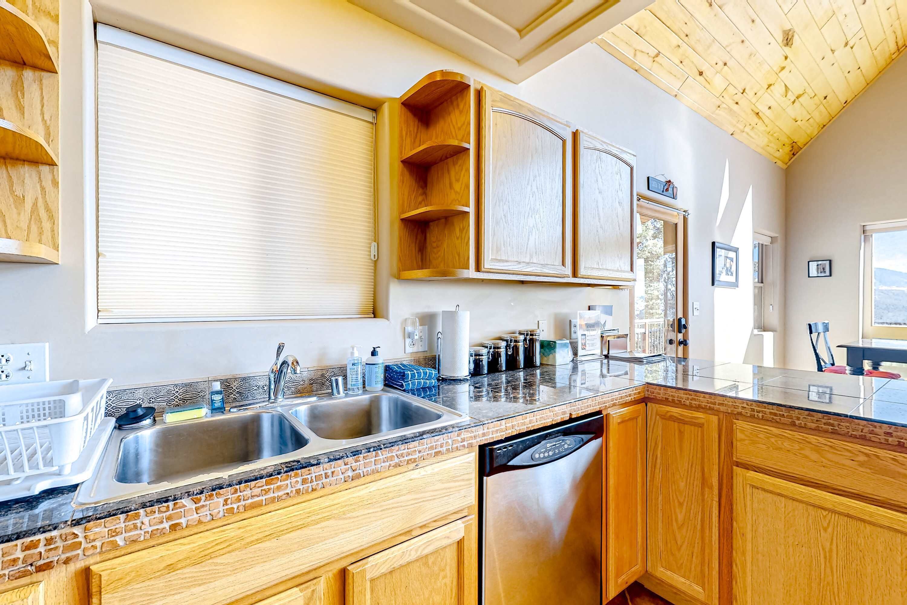 A kitchen with a double sink, wooden cabinets, a dishwasher, and a window with blinds.