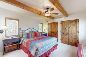 A bedroom with a bed, wooden ceiling beams, a ceiling fan, a nightstand, a lamp, a wicker basket, and wooden wardrobes. - Susan's Hideaway - Santa Fe Charm & Walk to Plaza (Santa Fe)