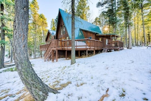 Eine Hütte mit steilem Dach, einer Holzterrasse und umgeben von Bäumen.