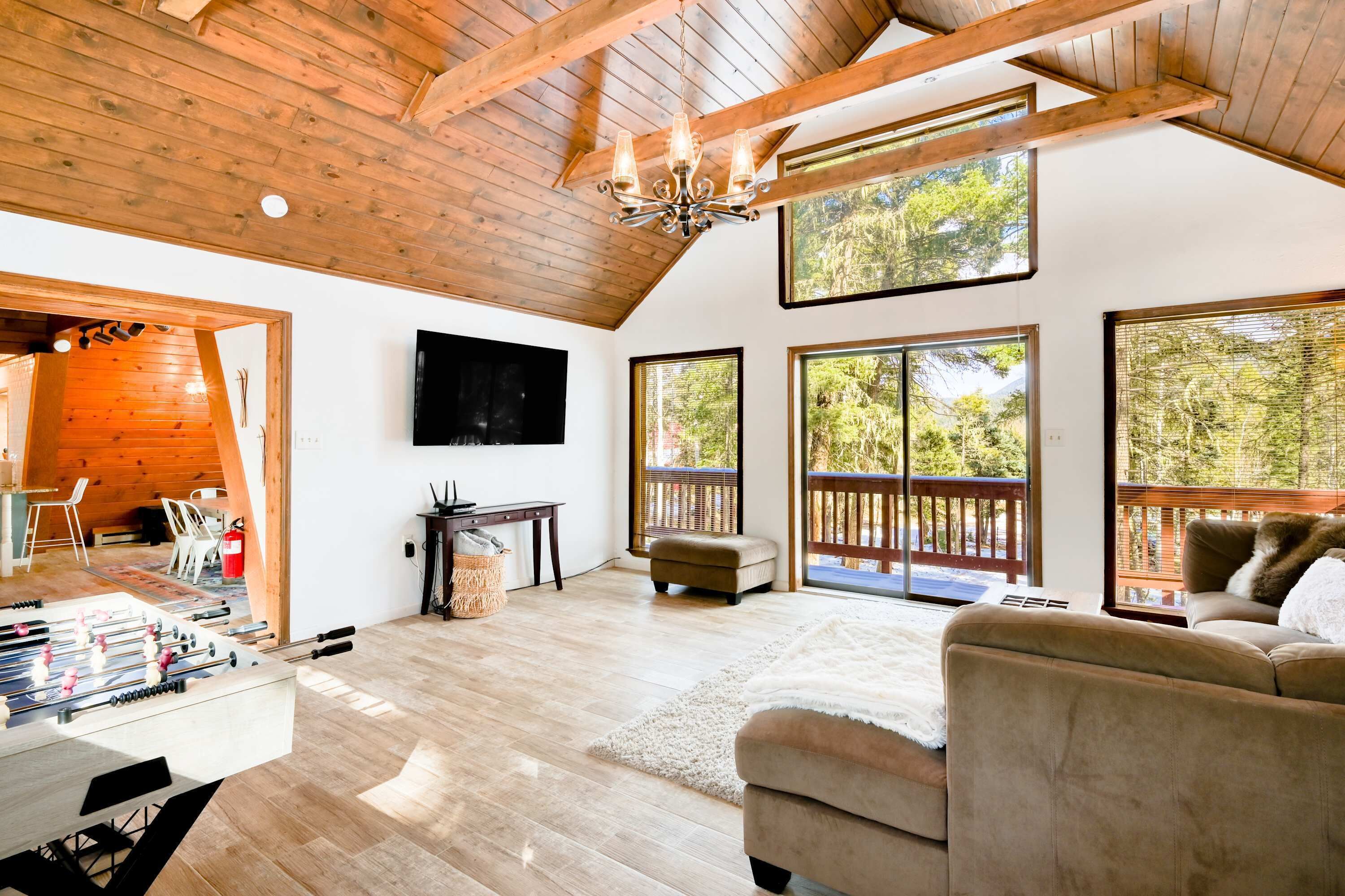 A spacious living area with a wooden ceiling, large windows, a sofa, and a foosball table.
