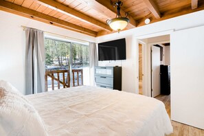 Ein Schlafzimmer mit einem großen Bett, einem Fernseher, einer Holzbalkendecke und Blick ins Freie.