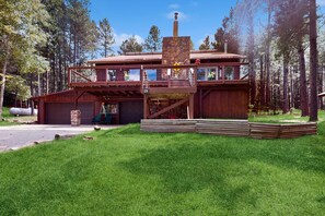 A two-story wooden cabin with a stone chimney, a balcony, and a garage. - Pine Valley Lodge - Views, Deck, Firepit & Sauna (Angel Fire)