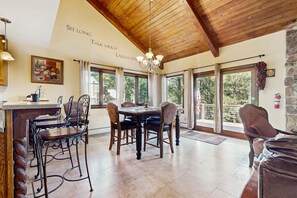 A dining area with a wooden ceiling, a chandelier, and a table with chairs. - Pine Valley Lodge - Views, Deck, Firepit & Sauna (Angel Fire)