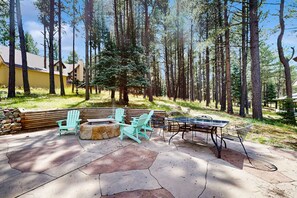 A patio with Adirondack chairs, a round table, and a ping pong table surrounded by a stone patio. - Pine Valley Lodge - Views, Deck, Firepit & Sauna (Angel Fire)