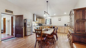 A spacious kitchen with wooden flooring, a dining table with chairs, and a large wooden cabinet. - Valley Views Cottage - Close to Ski Slopes & Town (Angel Fire)