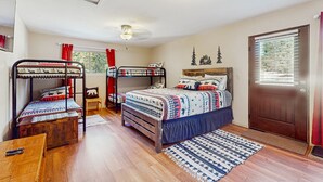 A room with bunk beds, a wooden table, a door, and a window with blinds. - Valley Views Cottage - Close to Ski Slopes & Town (Angel Fire)