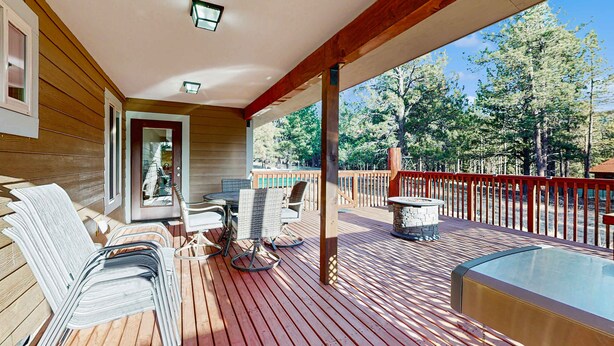 A wooden deck with outdoor furniture, a hot tub, and a view of trees. - Valley Views Cottage - Close to Ski Slopes & Town (Angel Fire)