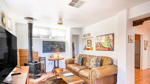 A living room with a sofa, a TV, a fireplace, and a painting on the wall. - Santa Fe Serenity - Walk to the Railyard, Dog-Friendly Garden Home (Santa Fe)