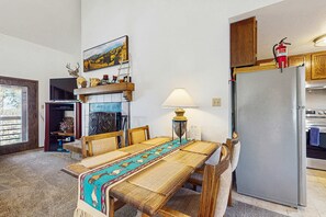Ein Essbereich mit Tisch, Stühlen, einer Lampe, einem Kühlschrank und einer Küchenzeile mit Schränken und einem Herd.