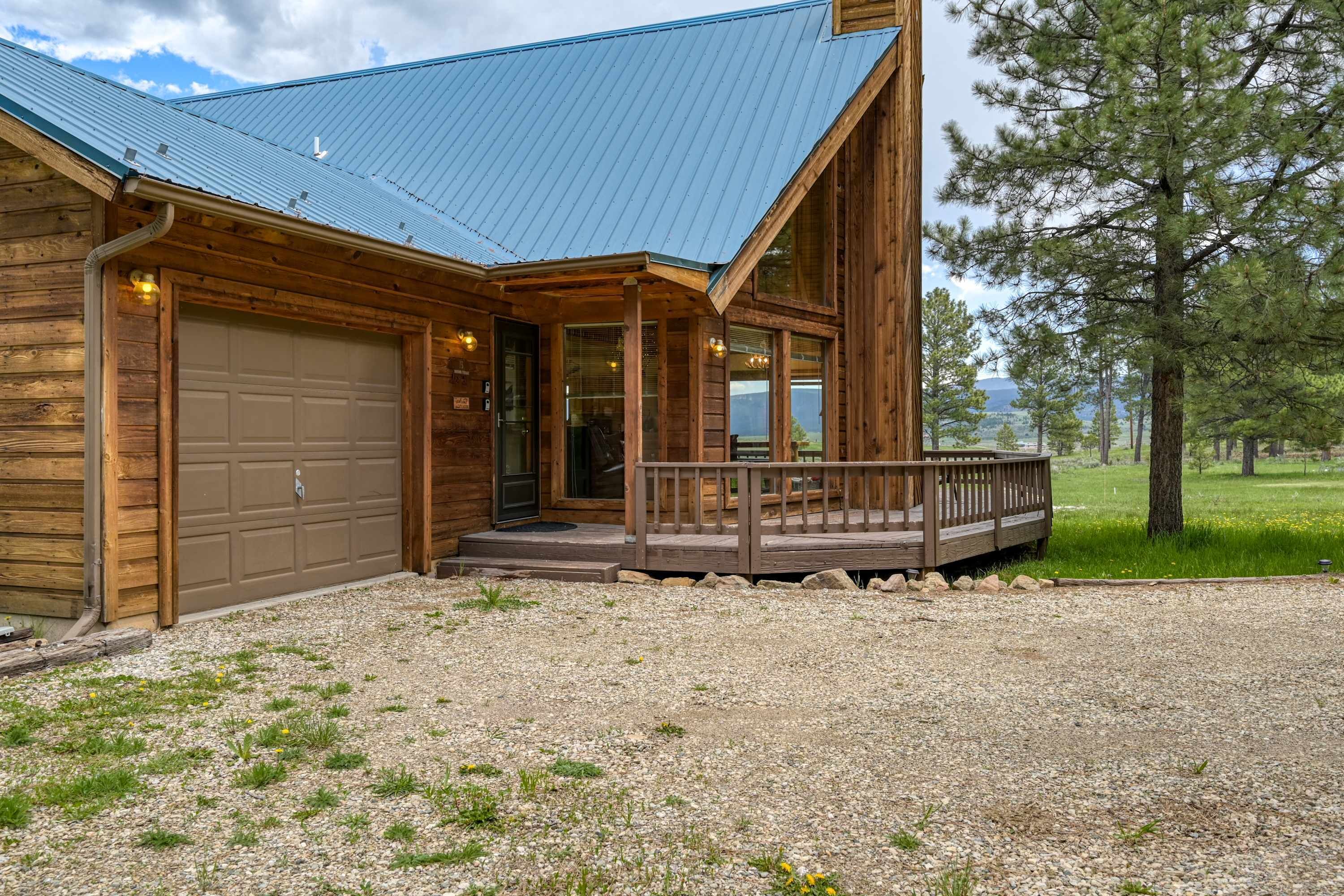 Una cabaña de troncos con techo de metal, un porche delantero y un camino de entrada de grava.
