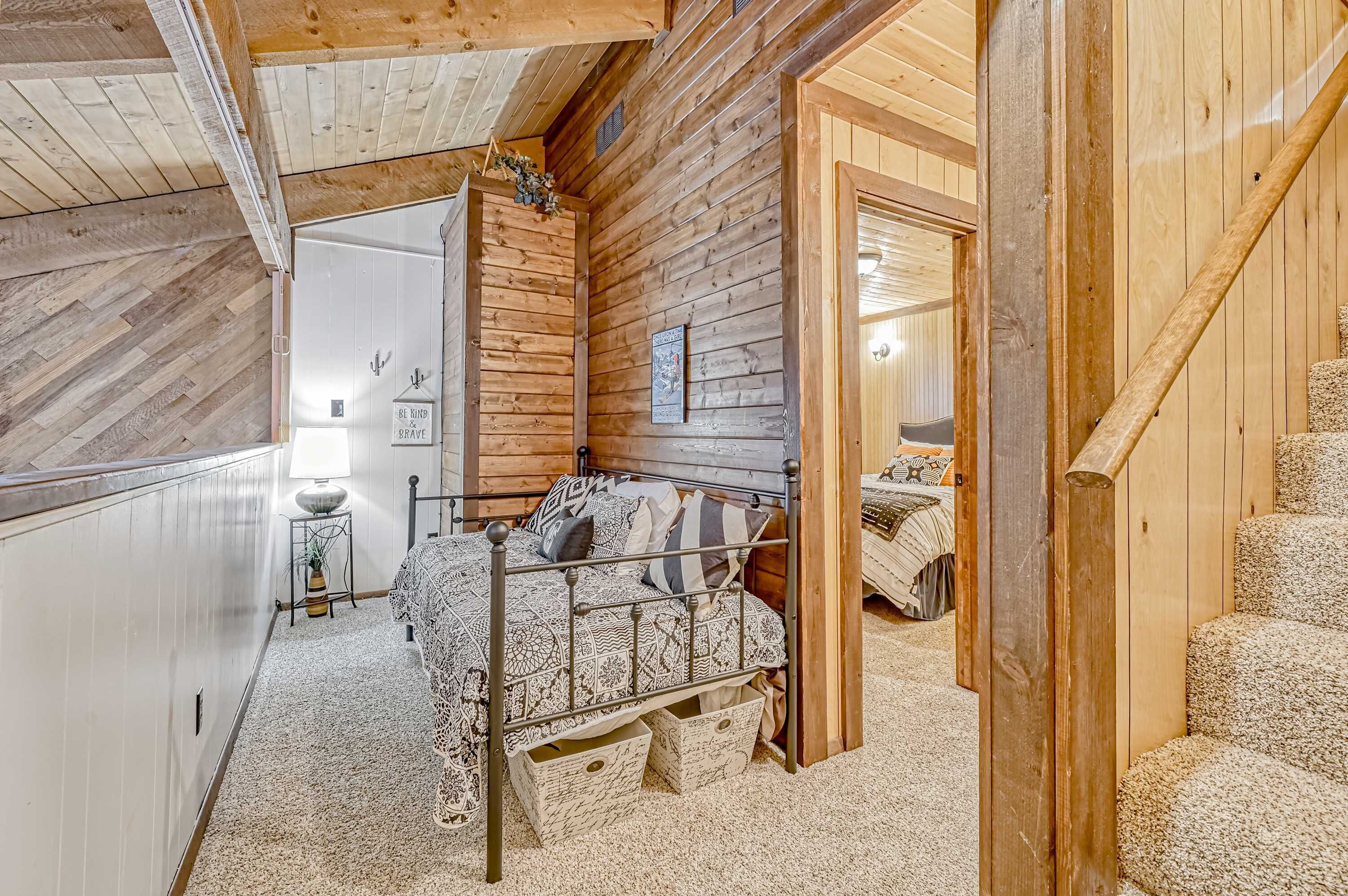 A wooden cabin bedroom with a metal bed frame, a small bedside table, and a door leading to another room.