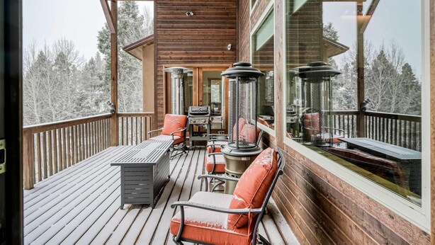 A wooden deck with outdoor furniture, including chairs and a table, and a large window offering a view of snow-covered trees. - Vista Linda Cabin - Views, Sauna, Deck & Dog Okay (Angel Fire)