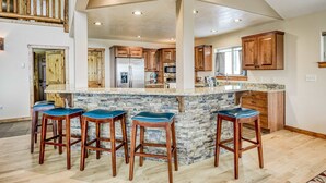 A spacious kitchen with a central island, wooden bar stools, and a stone backsplash. - Vista Linda Cabin - Views, Sauna, Deck & Dog Okay (Angel Fire)