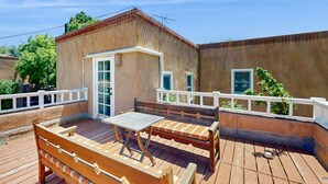 Un patio con una panca e un tavolo in legno, una piccola porta bianca e una ringhiera bianca.