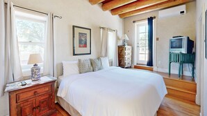 Una camera da letto con un letto grande, travi in legno a soffitto, un comò, una televisione e una finestra con tende.