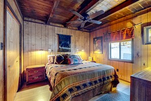 A wooden-paneled bedroom with a bed, nightstands, a ceiling fan, and a window.