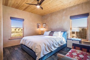 Ein Schlafzimmer mit einem Bett, zwei Fenstern, einem Deckenventilator und einem Nachttisch mit Lampe.