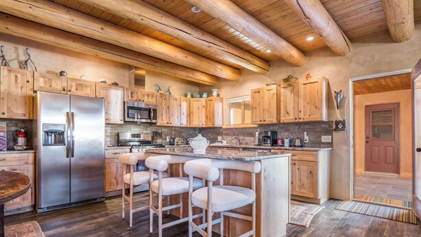 Una cucina con mobili in legno, un frigorifero in acciaio inossidabile, un angolo bar con sgabelli e una grande isola.