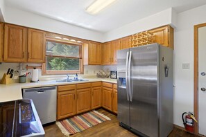A kitchen with wooden cabinets, stainless steel appliances, a dishwasher, and a window with blinds. - Snowfire 312A - Walk to Ski, Hike, Bike & Dining (Angel Fire)