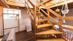 Una escalera de madera en una habitación con una ventana, una mesita y una cesta colgante.